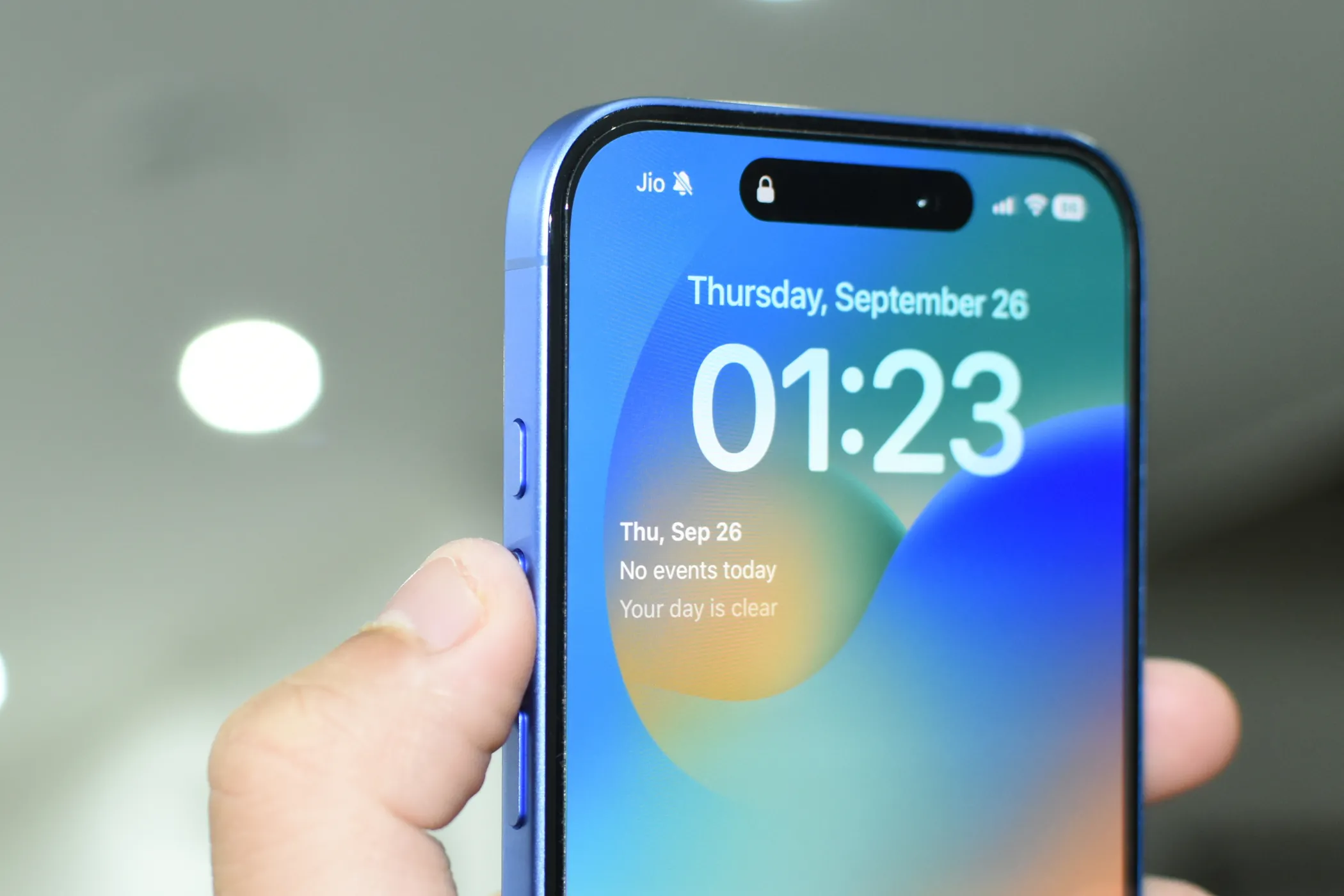 Chiếc iPhone 16 màu Ultramarine với ngón tay chỉ vào Nút Tác Vụ (Action Button), gợi ý khả năng kích hoạt Chế độ hoảng loạn.