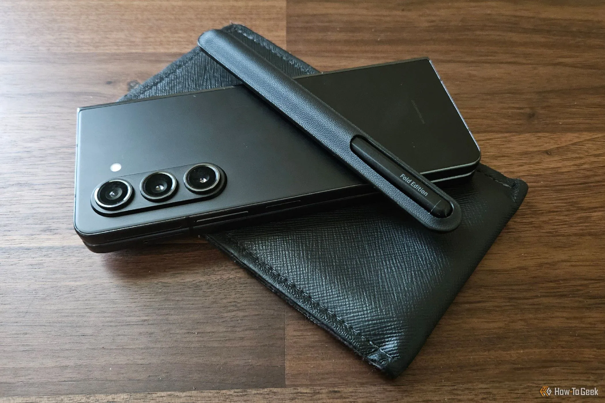 Điện thoại Samsung Galaxy Z Fold 5 màu đen được đặt trong một bao da bảo vệ có túi đựng bút S Pen, thể hiện cách người dùng mang theo bút cảm ứng lớn.
