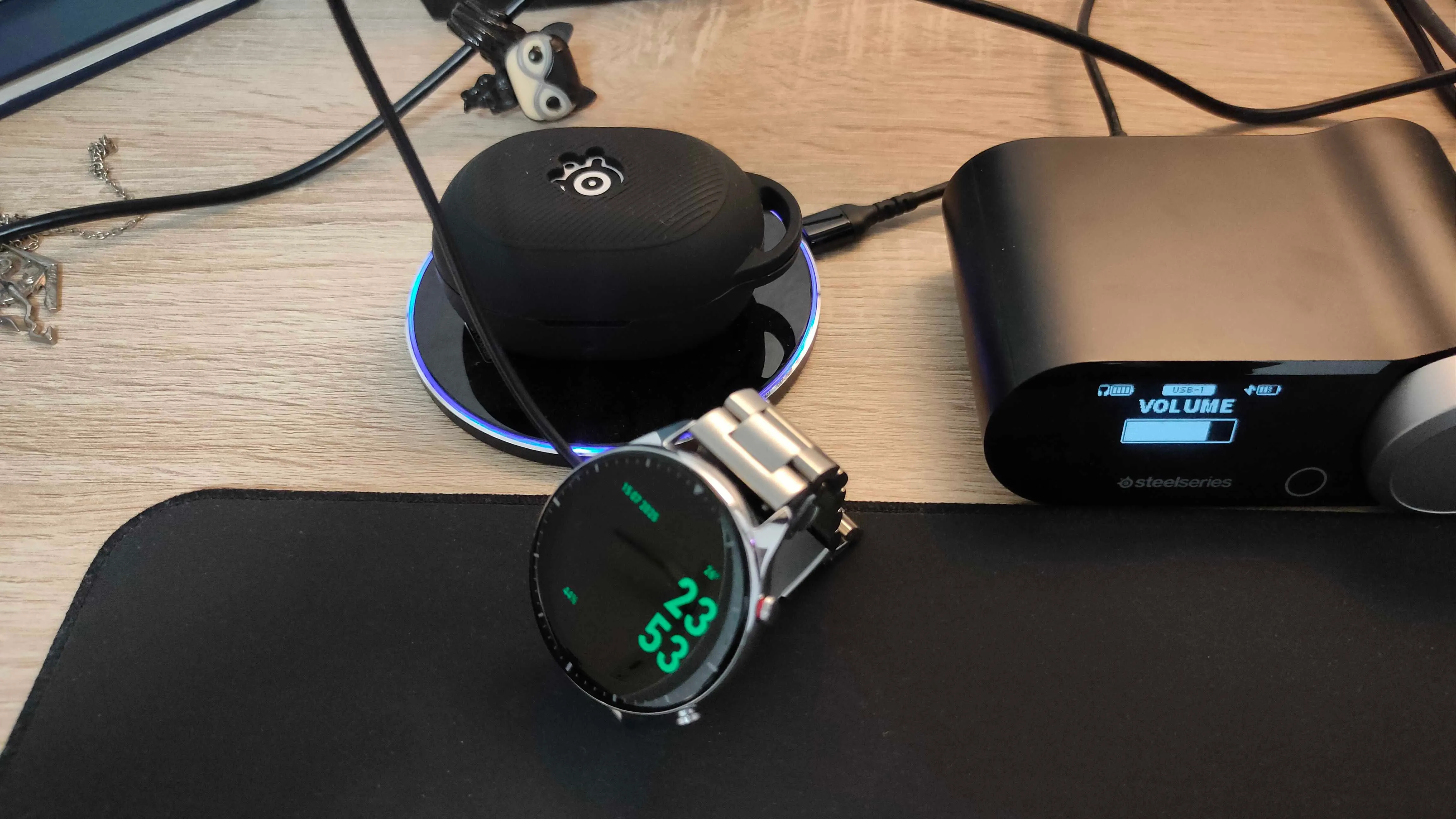 Đồng hồ thông minh Amazfit GTR 2 và tai nghe không dây SteelSeries Arctis GameBuds đang sạc trên bàn làm việc, minh họa khả năng sạc thiết bị qua cổng USB màn hình.