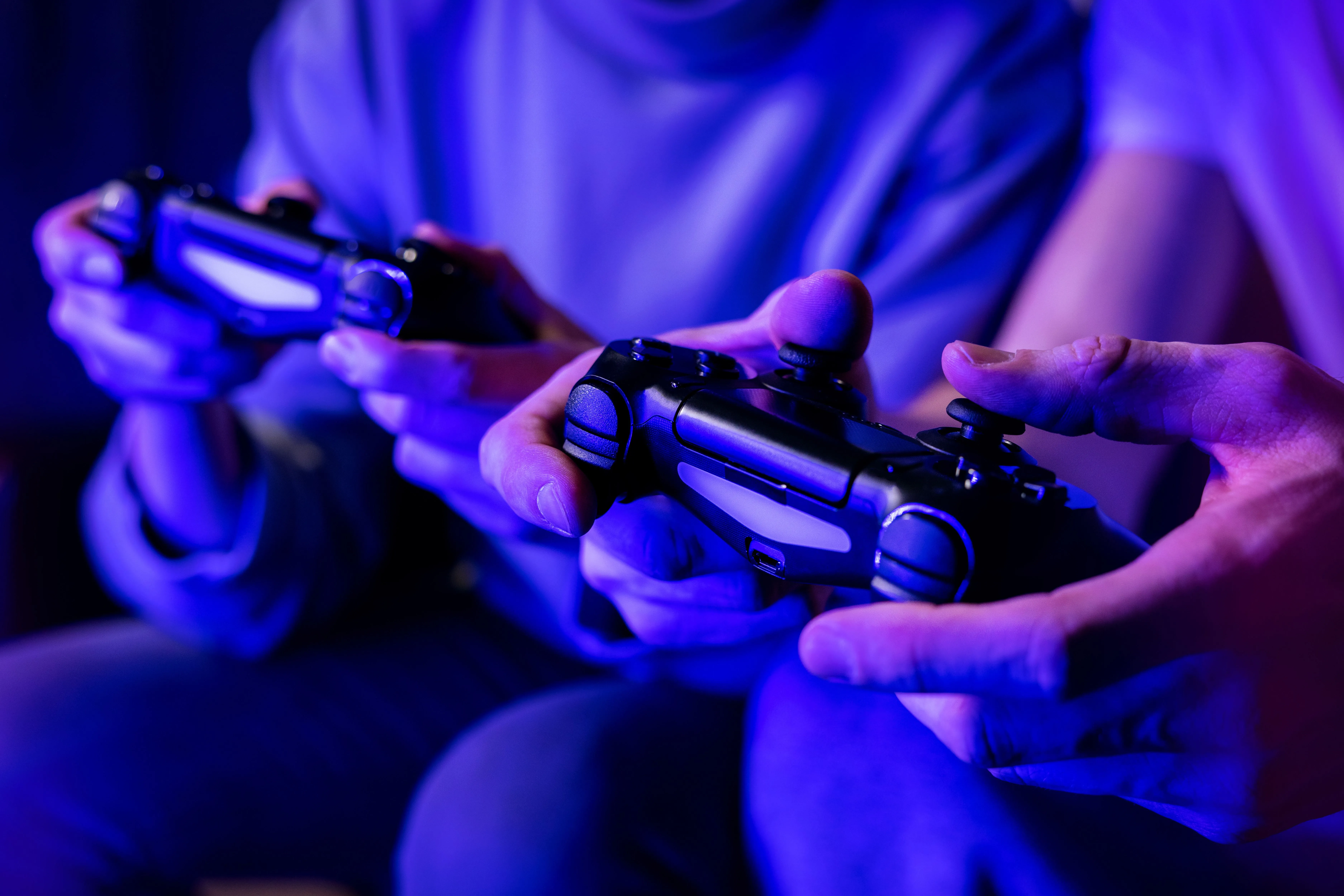 Hai người bạn đang cùng nhau chơi game multiplayer trên sofa, mỗi người một tay cầm, minh họa nhu cầu về gói PS Plus chỉ dành riêng cho chế độ trực tuyến.