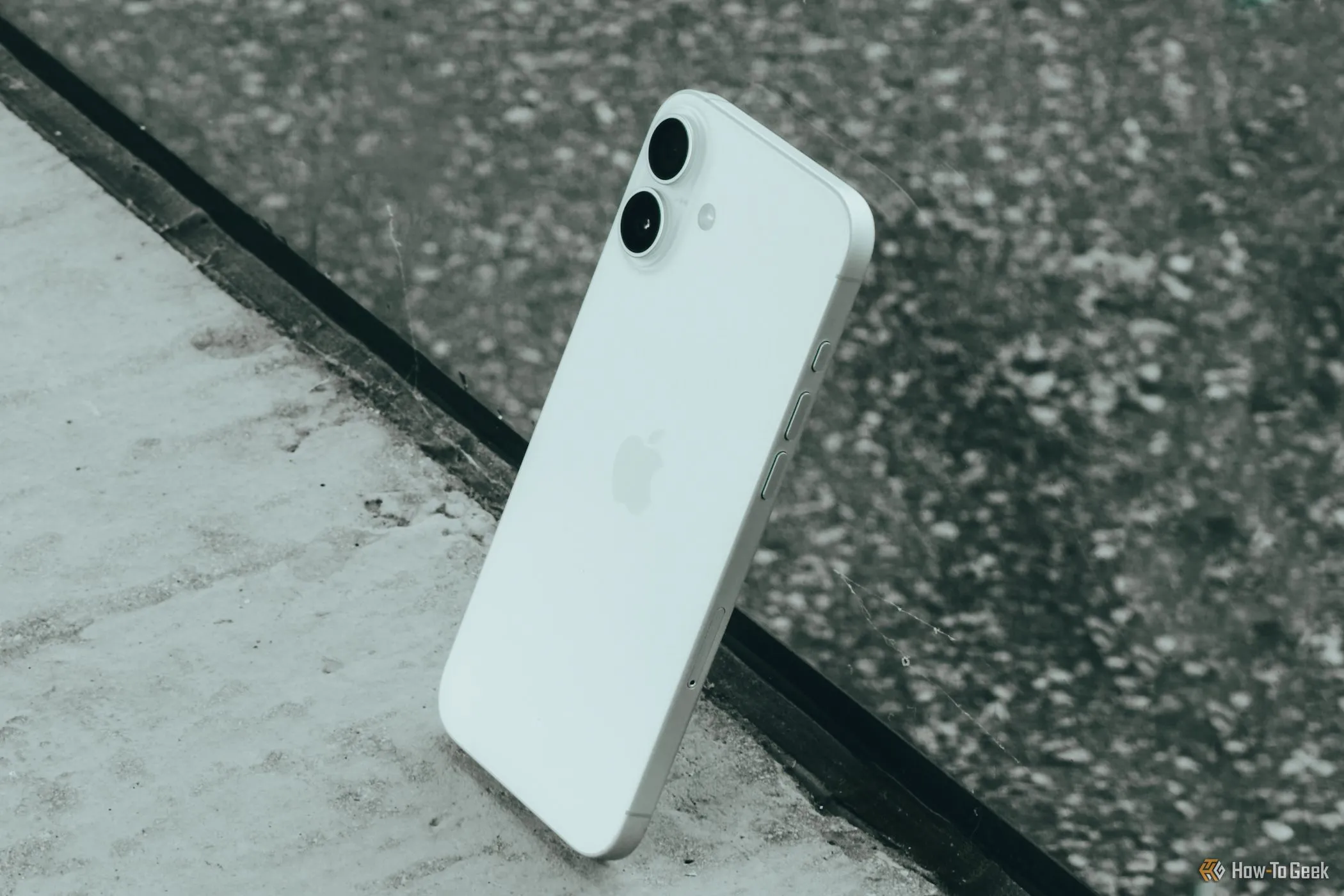 Hình ảnh iPhone 16 Plus được đặt nghiêng cạnh bề mặt kính, làm nổi bật thiết kế và các ống kính camera