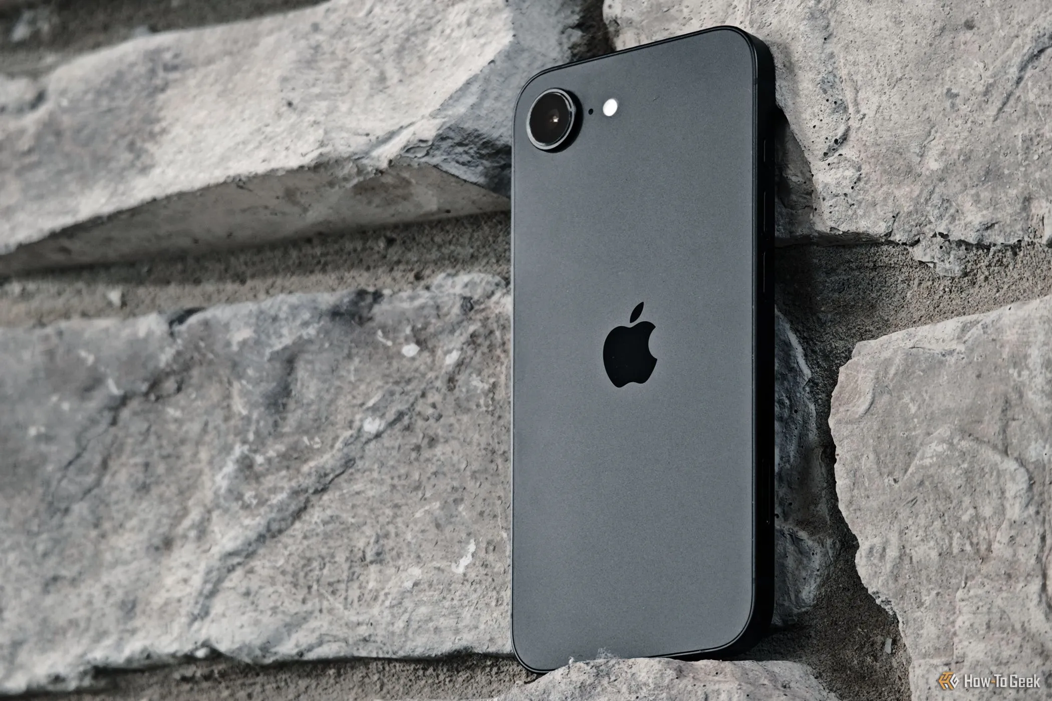 iPhone 16e màu đen được đặt nghiêng trên nền tường gạch, nổi bật thiết kế tối giản