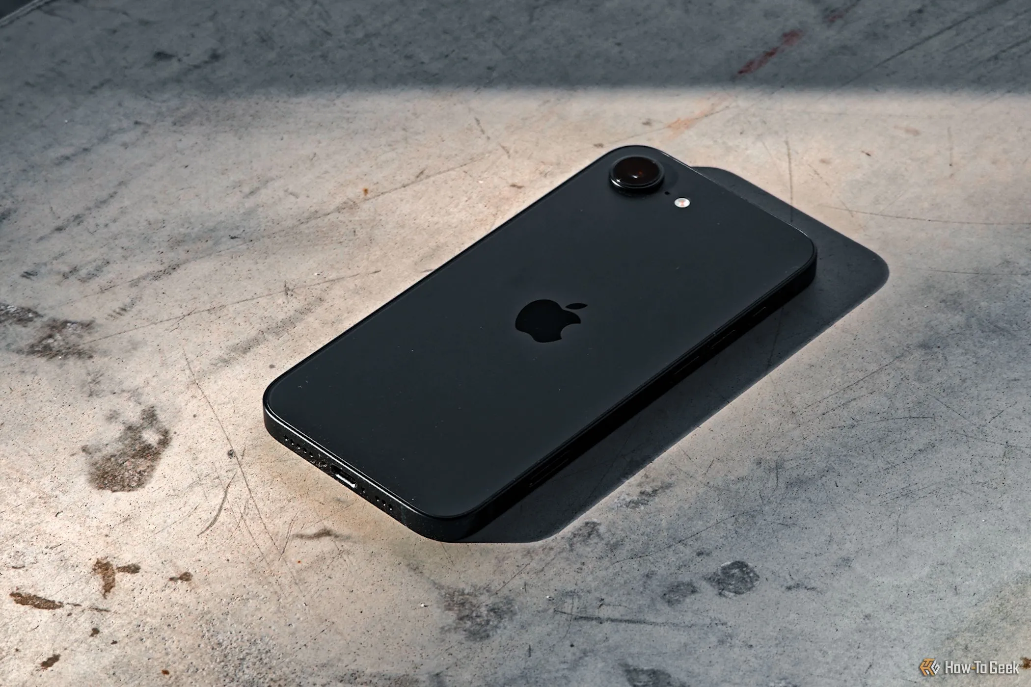 iPhone 16e màu đen được đặt úp trên bề mặt bê tông, làm nổi bật mặt lưng tối giản