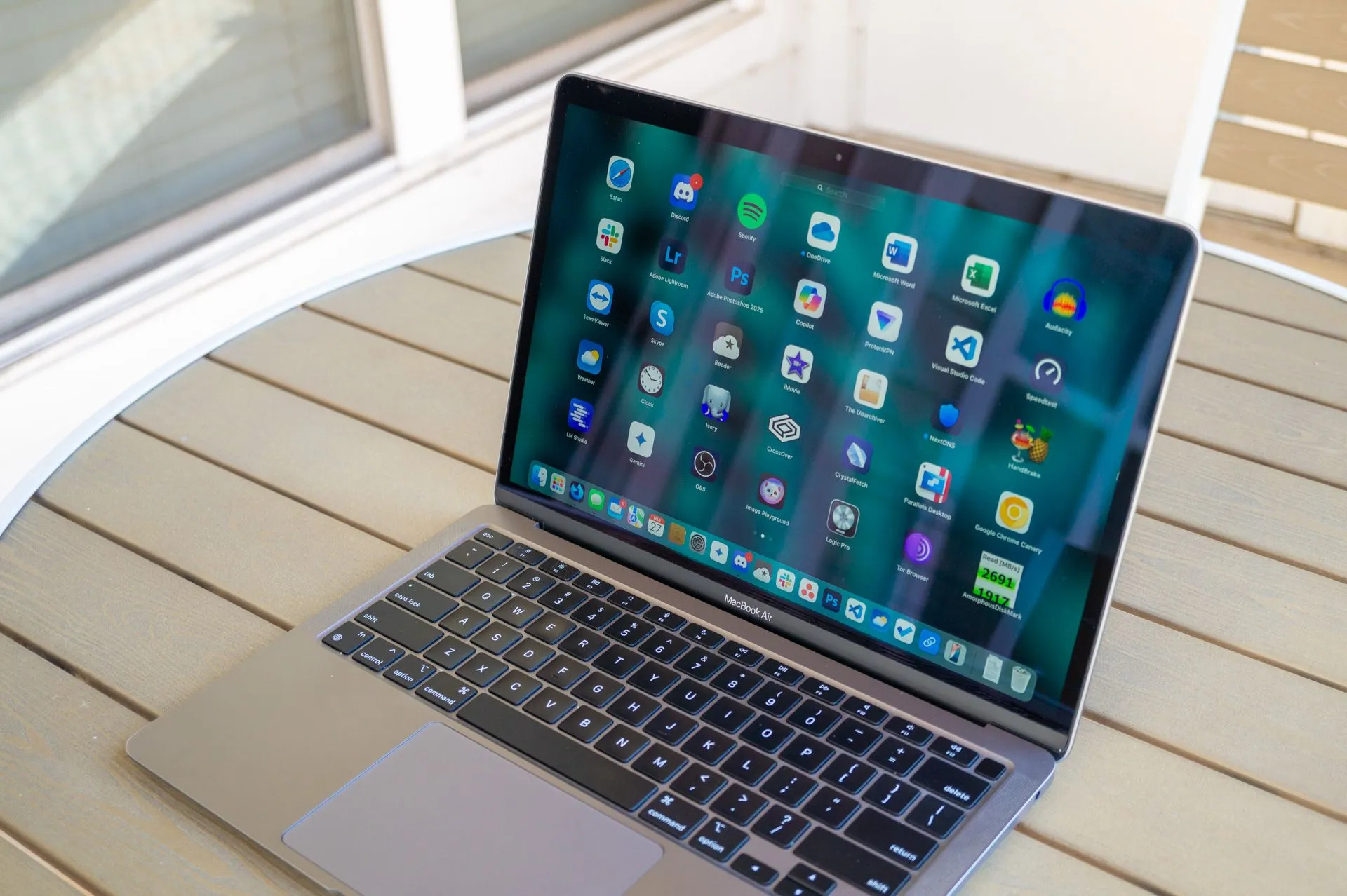 MacBook Air với ứng dụng Launchpad đang mở, đặt trên bàn ngoài hiên nhà.