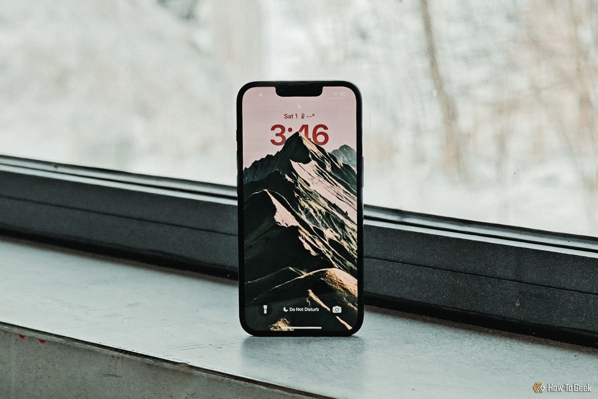Màn hình khóa iPhone 16e hiển thị rõ nét đặt trước khung cửa sổ, ánh sáng tự nhiên làm nổi bật chất lượng hiển thị