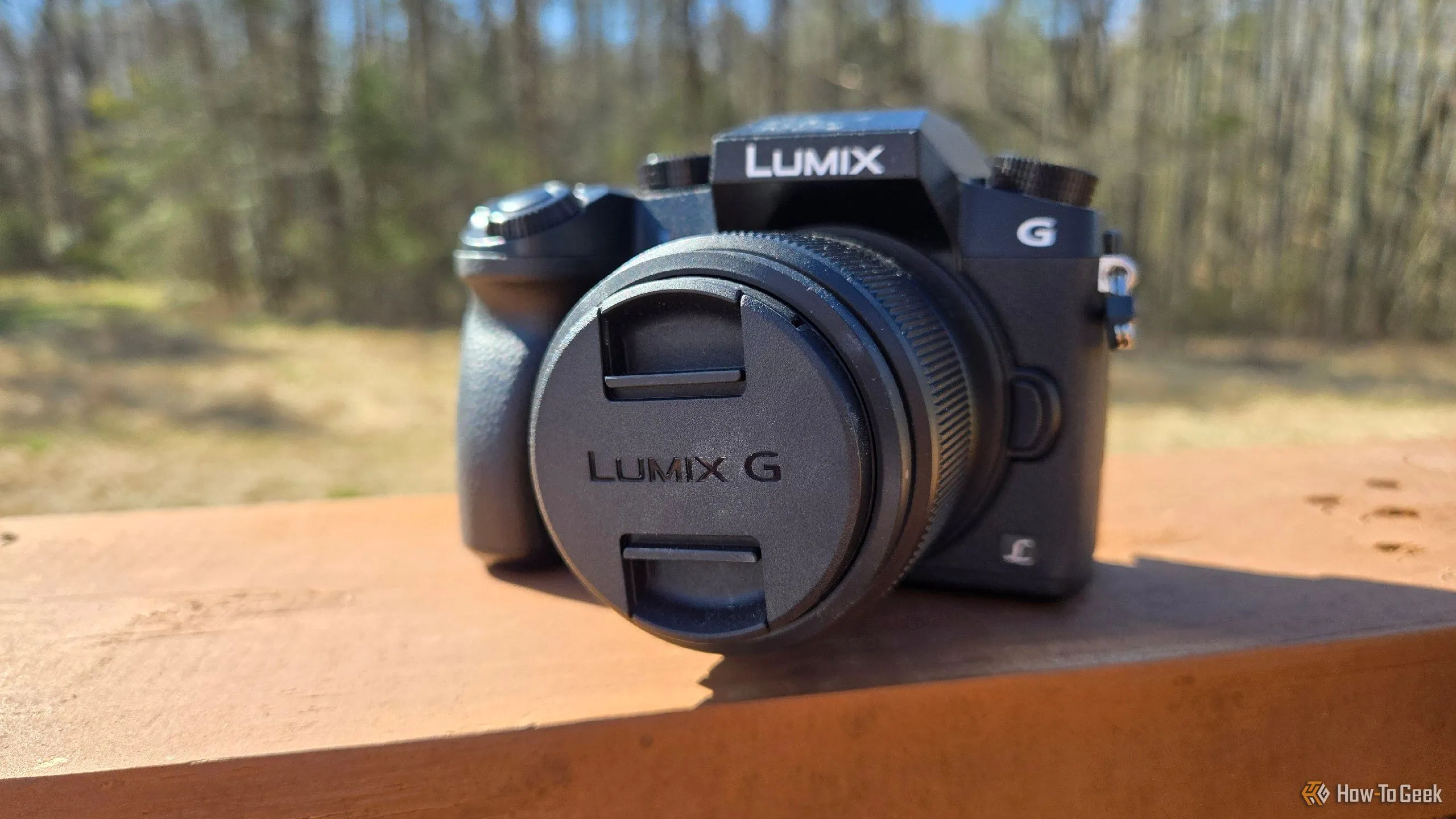 Máy ảnh mirrorless Panasonic Lumix G7 đời 2015 đặt trên lan can, được so sánh với khả năng chụp ảnh của điện thoại thông minh hiện đại.