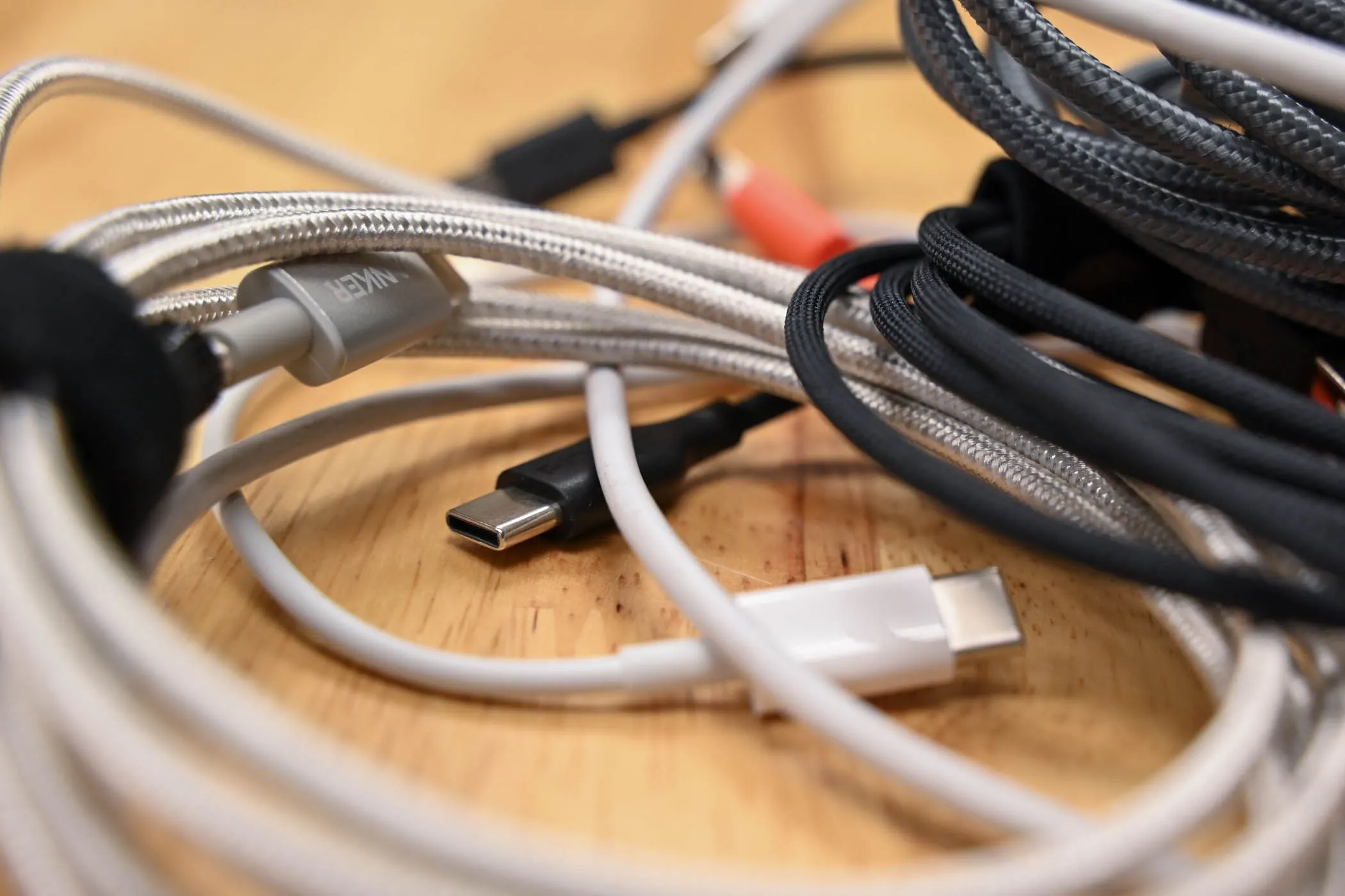 Một chồng cáp USB-C các loại trên bề mặt gỗ, tượng trưng cho sự đa dạng cáp sạc hiện nay.