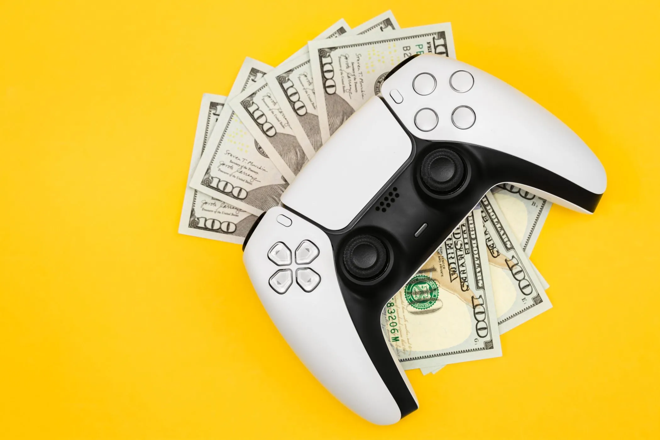Năm tờ 100 đô la Mỹ được đặt dưới một tay cầm PlayStation 5, tượng trưng cho chi phí phát triển và giá thành game ngày càng cao.