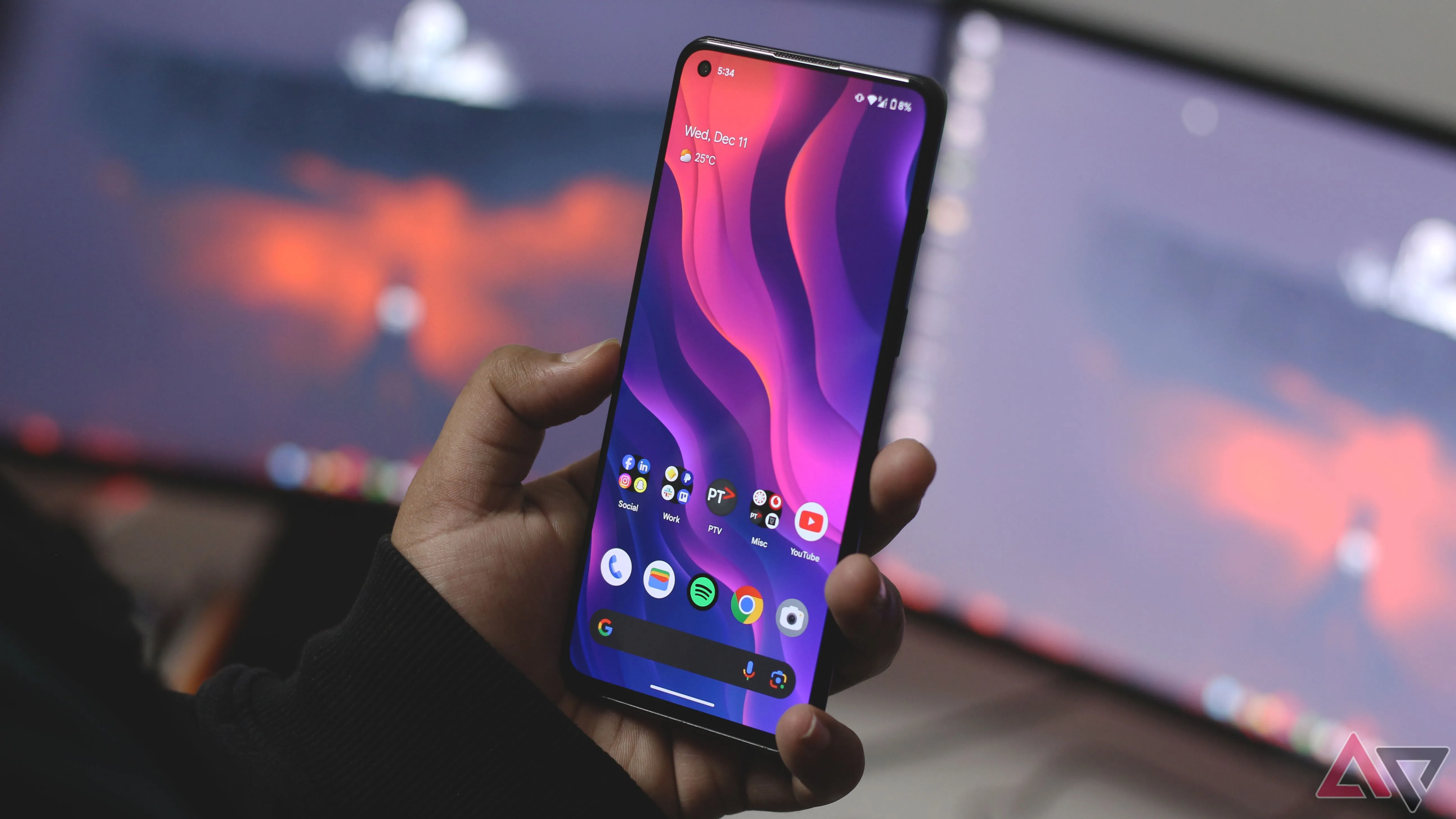 Người dùng cầm điện thoại Android trên bàn làm việc có nhiều màn hình máy tính, minh họa trải nghiệm điều hướng trên thiết bị di động