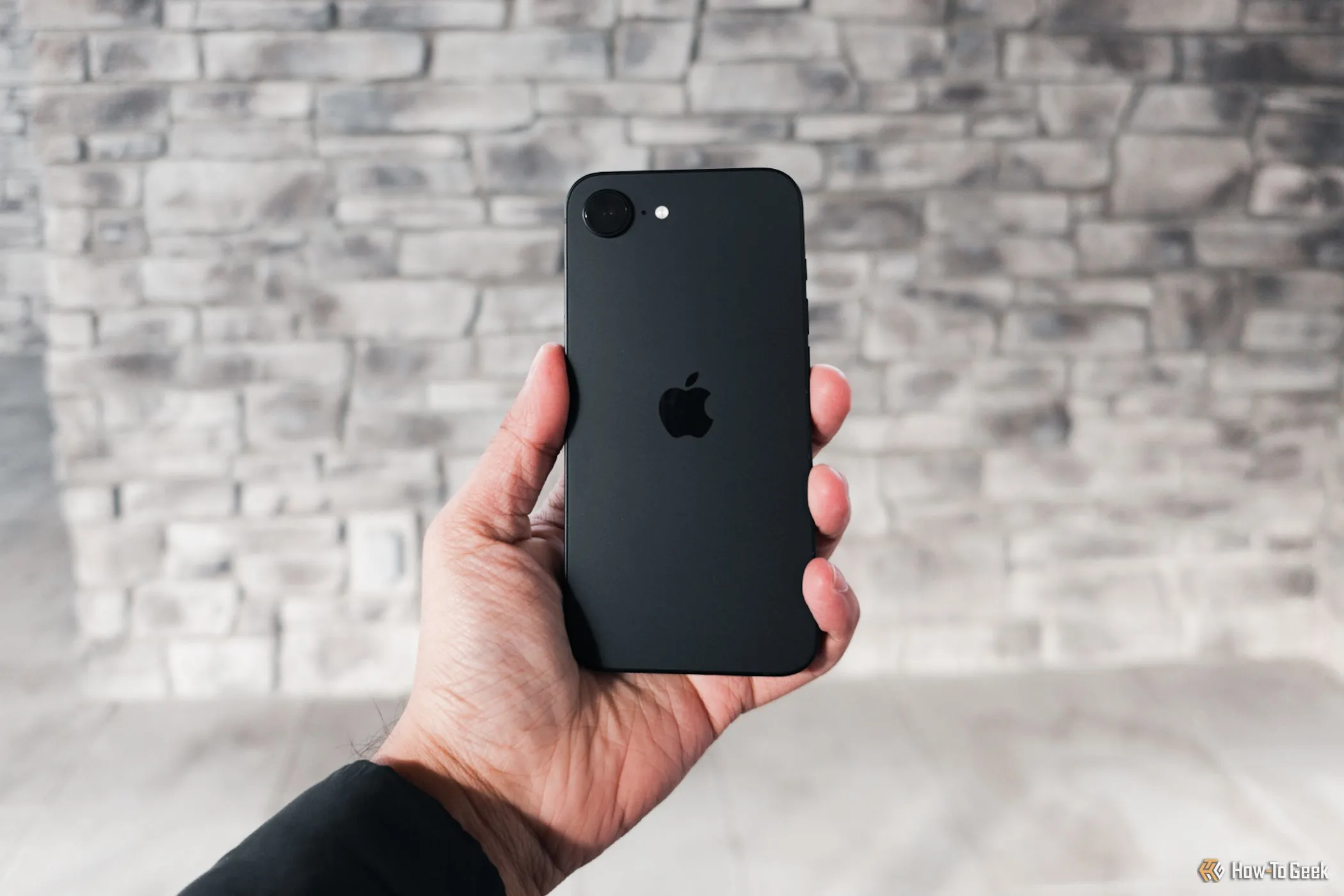 Người dùng cầm iPhone 16e trên tay với phông nền tường xám, thể hiện kích thước vừa vặn