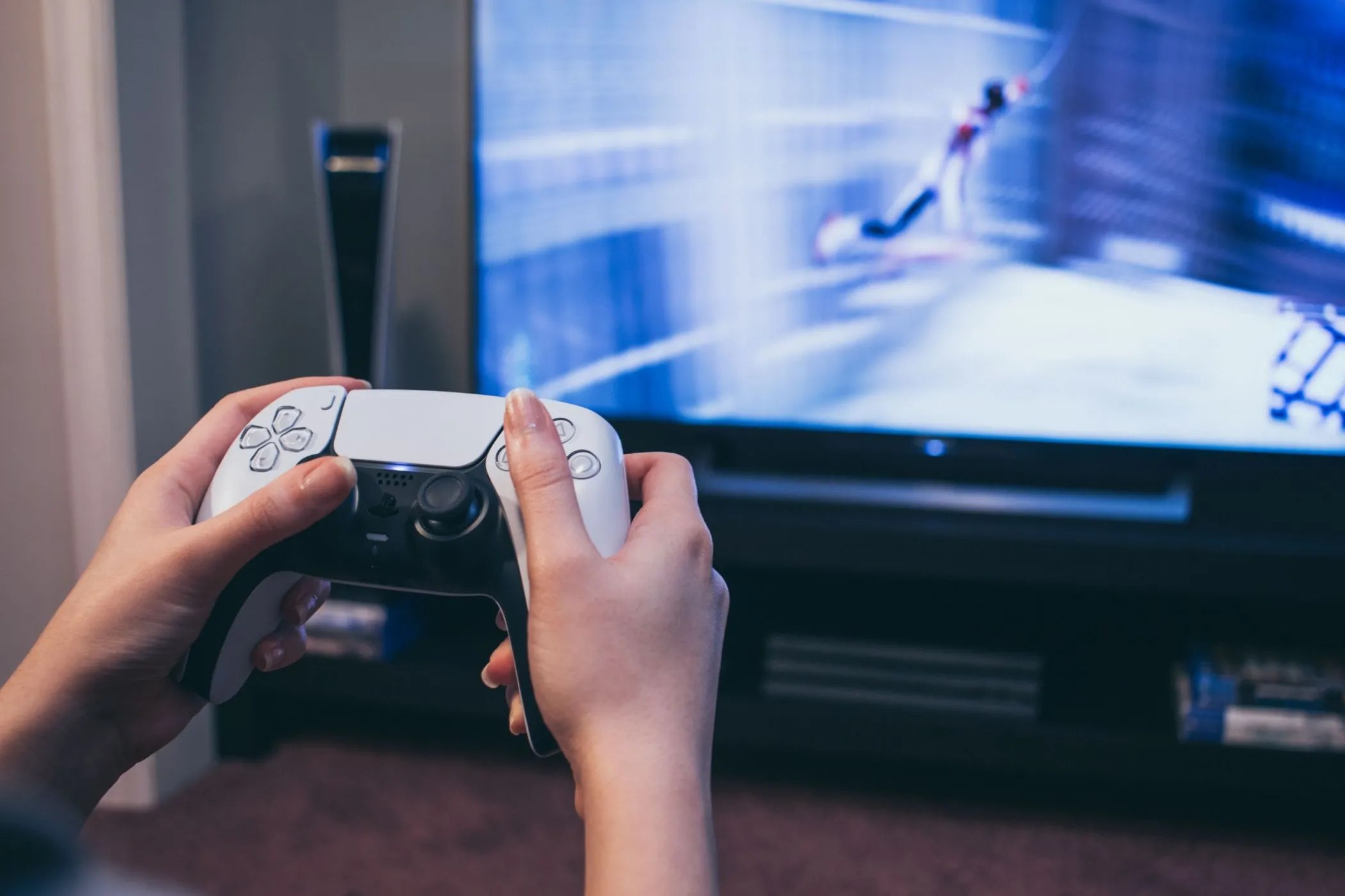 Tay người chơi cầm bộ điều khiển DualSense của PS5 trước màn hình TV hiển thị game Spider-Man, minh họa tính năng chia sẻ game và tài khoản PlayStation Plus.