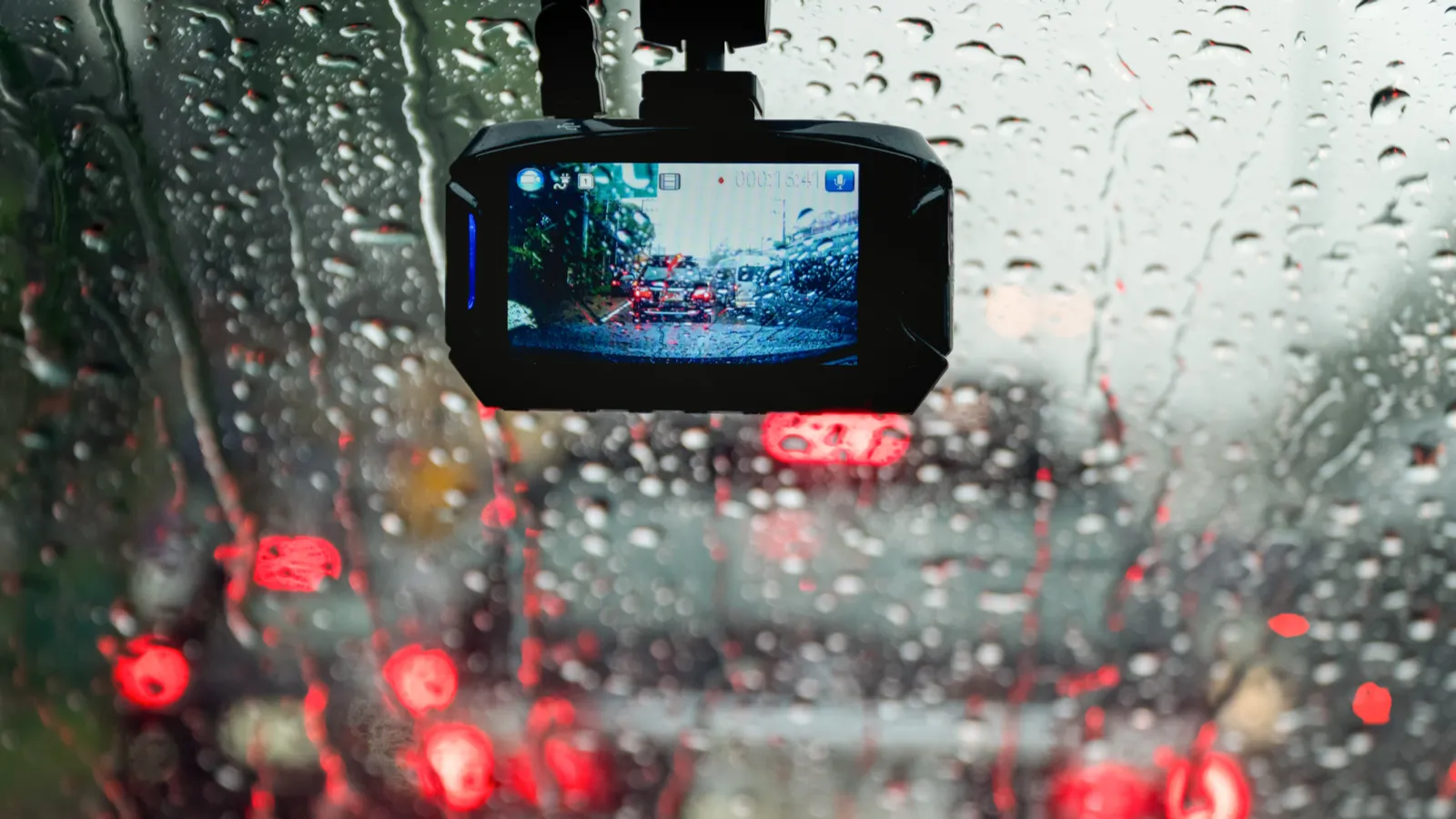 Thiết bị camera hành trình đang ghi hình trên kính chắn gió ô tô trong điều kiện mưa, so sánh với tiềm năng iPhone làm dashcam.