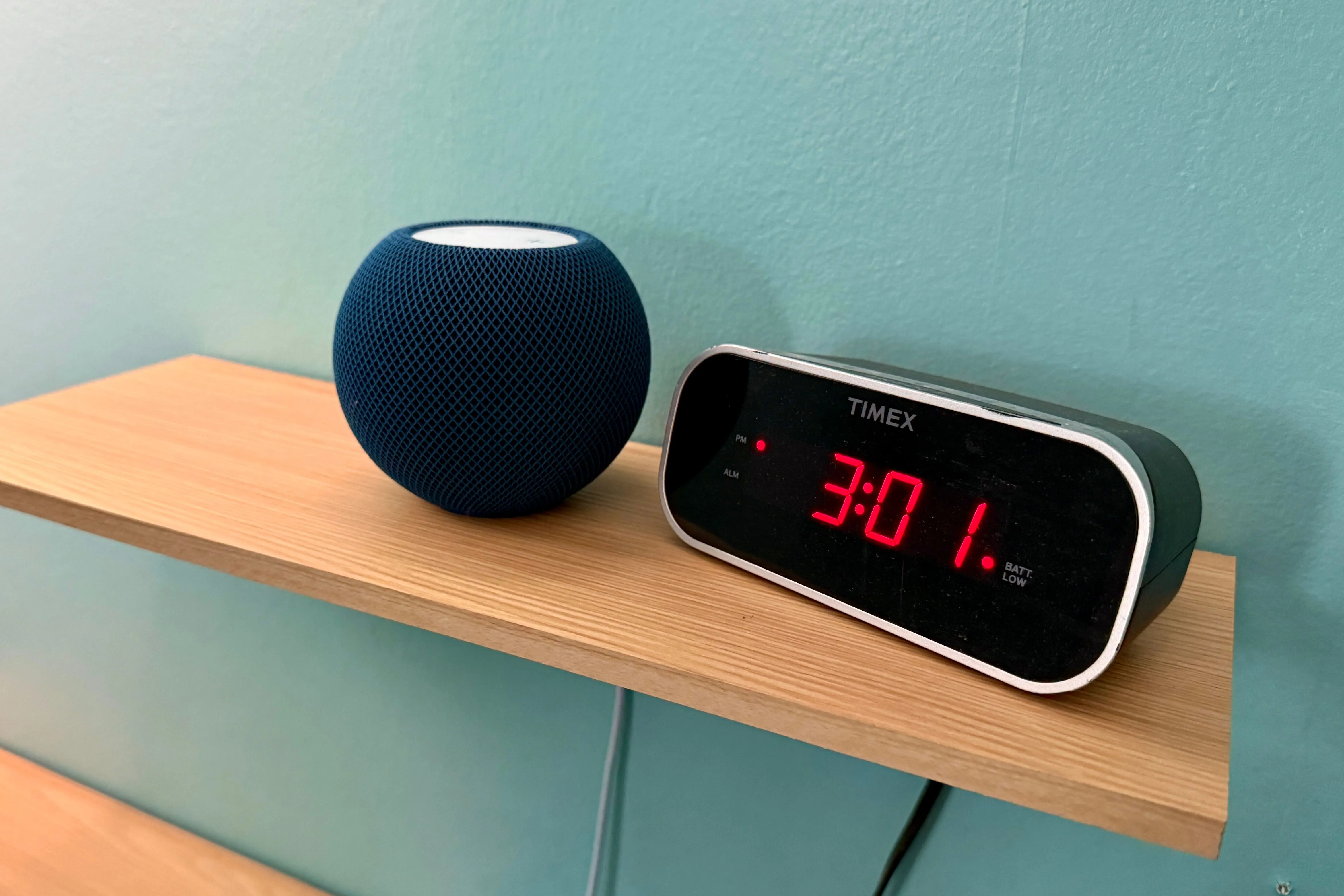 Apple HomePod mini màu xám không gian đặt cạnh một chiếc đồng hồ điện tử, mang đến âm thanh sống động.