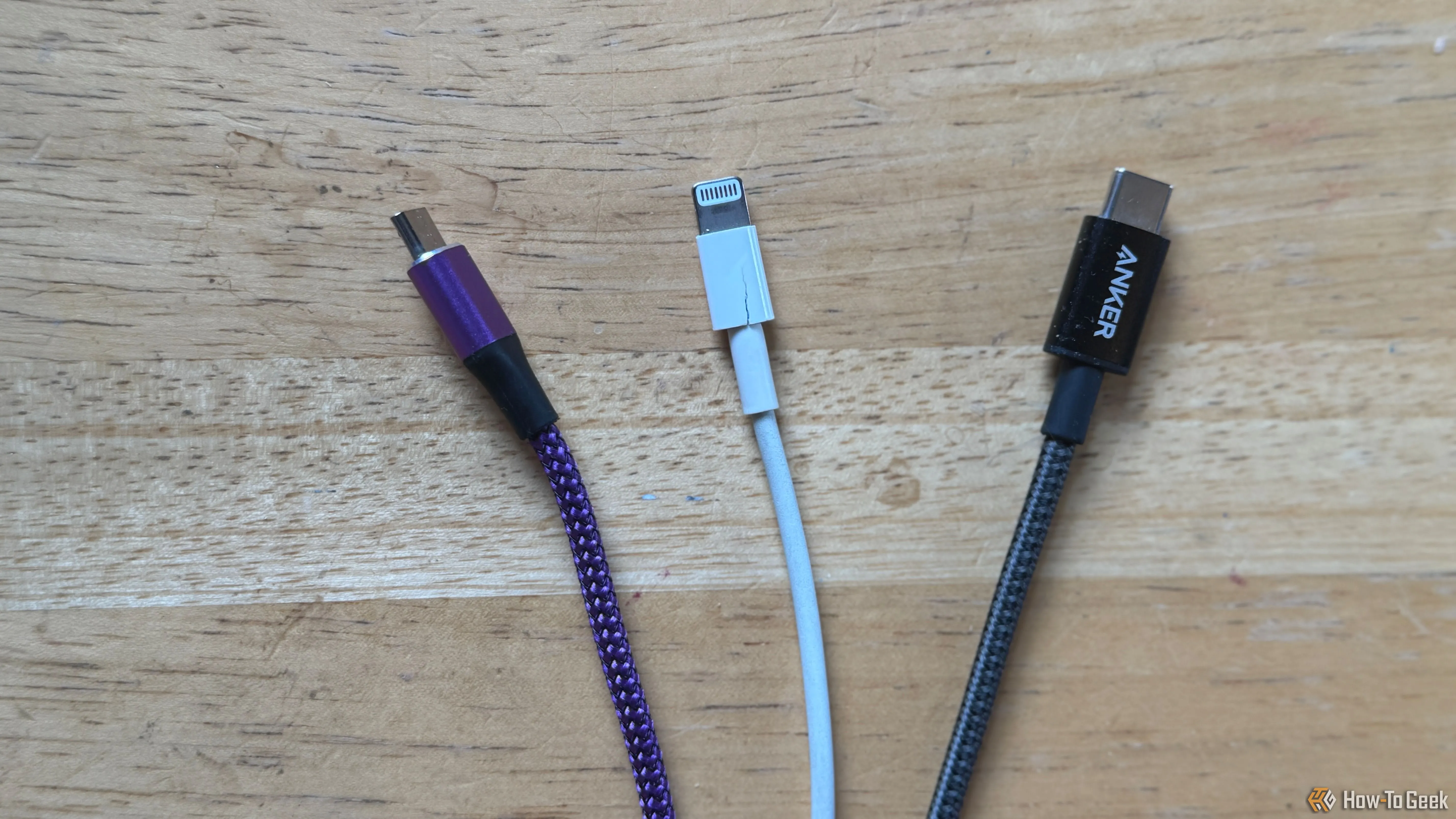 Các loại cáp sạc phổ biến: cáp micro-USB màu tím, cáp Lightning màu trắng và cáp USB-C màu xám trên mặt bàn