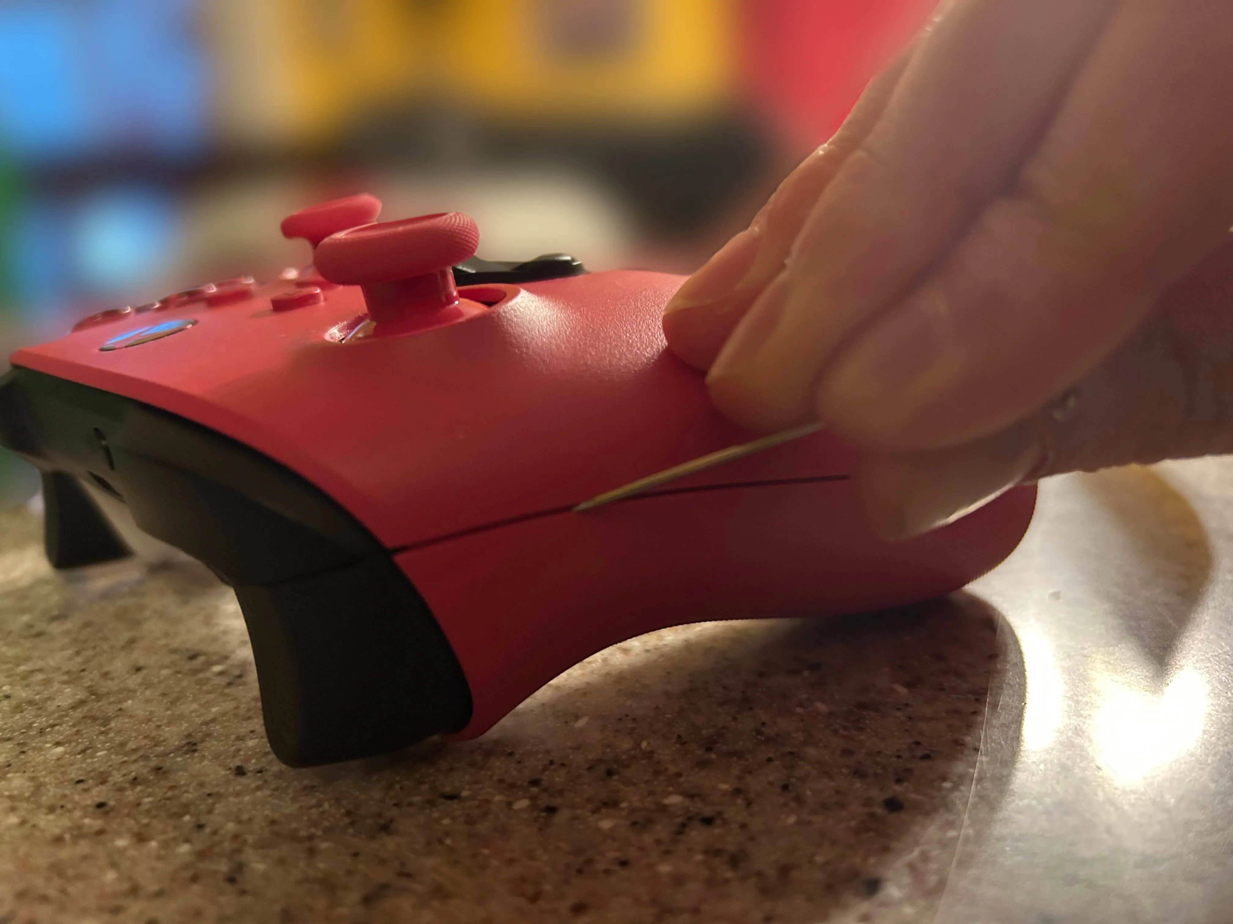 Dùng dụng cụ kim loại mỏng làm sạch bụi bẩn và da chết ở khe nối của tay cầm Xbox màu hồng