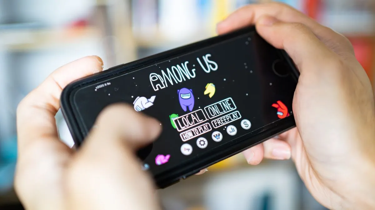 Hình ảnh cận cảnh hai bàn tay đang chơi game Among Us trên điện thoại thông minh, minh họa cho trải nghiệm chơi co-op cục bộ phổ biến trên di động.