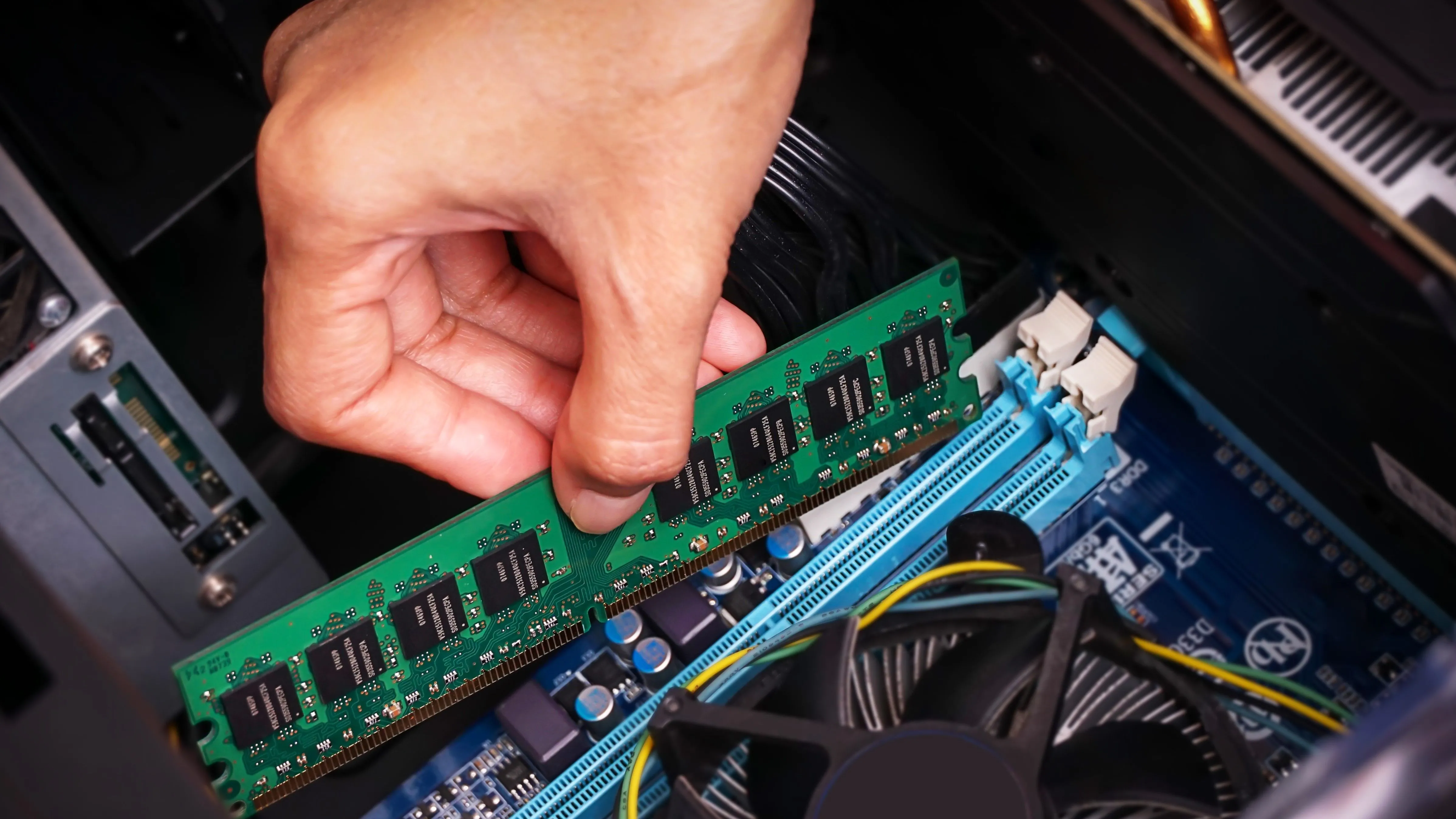 Hình ảnh một bàn tay đang nhấn thanh RAM vào vị trí trong một chiếc PC để bàn, nhấn mạnh quá trình lắp đặt và nâng cấp RAM, một thành phần quan trọng đối với hiệu suất máy tính.