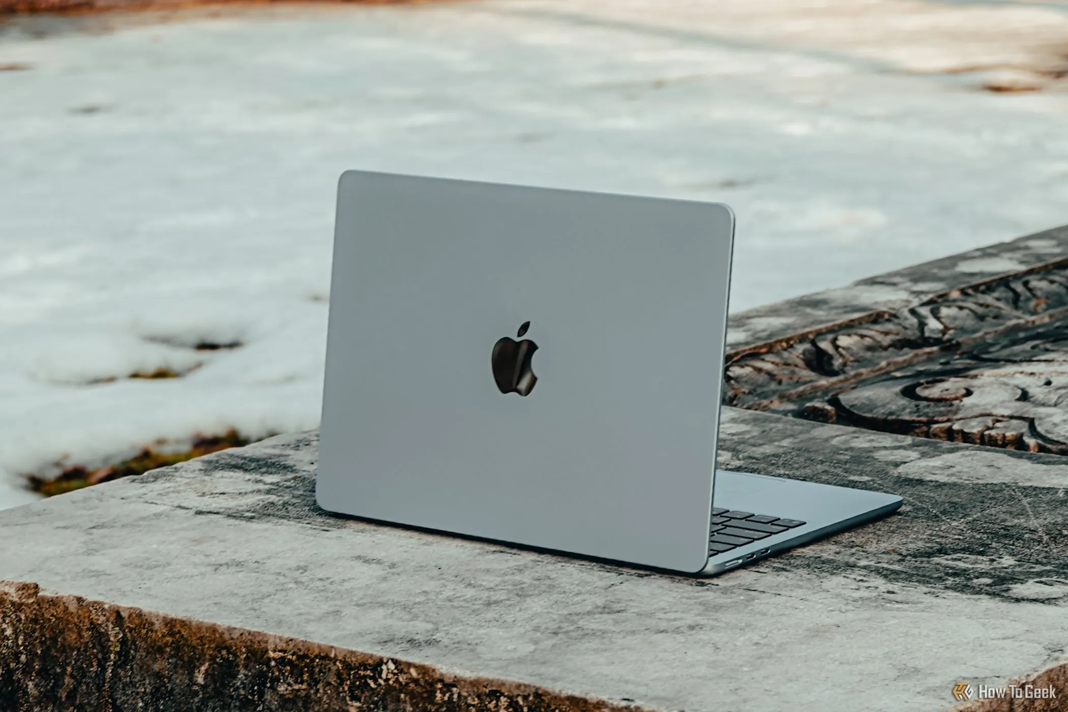 MacBook Air M4 màu xanh lam đặt trên ghế đá, thể hiện thiết kế sang trọng nhưng vẫn khó sửa chữa