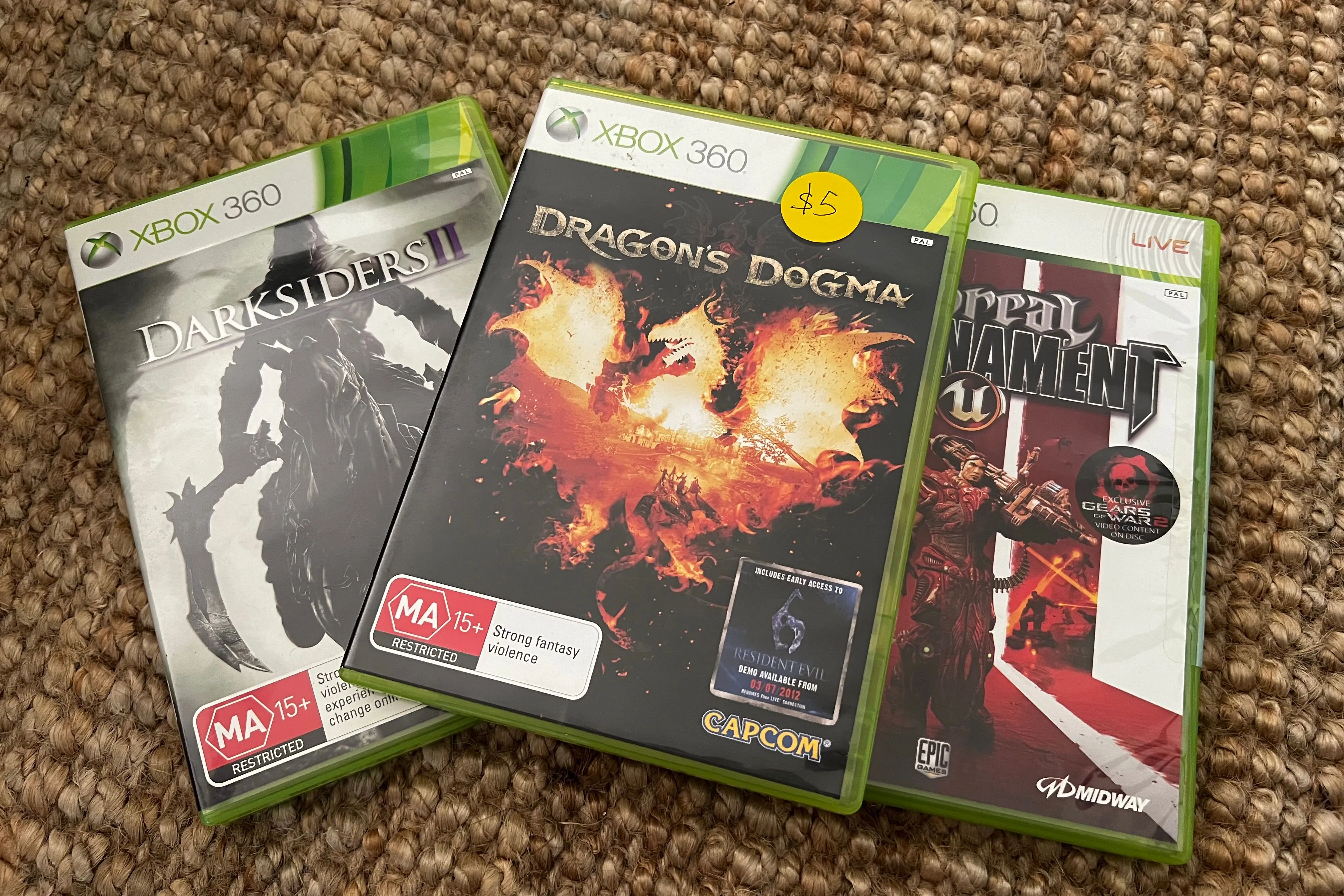 Một chồng đĩa game cũ, bao gồm Dragon Age Inquisition, tượng trưng cho thị trường game đã qua sử dụng với giá phải chăng