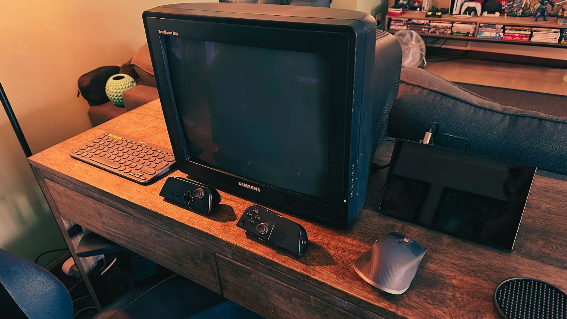 Một màn hình máy tính CRT đang kết nối với một PC cầm tay, kèm theo chuột và bàn phím trên bàn làm việc cùng một số bộ điều khiển chơi game