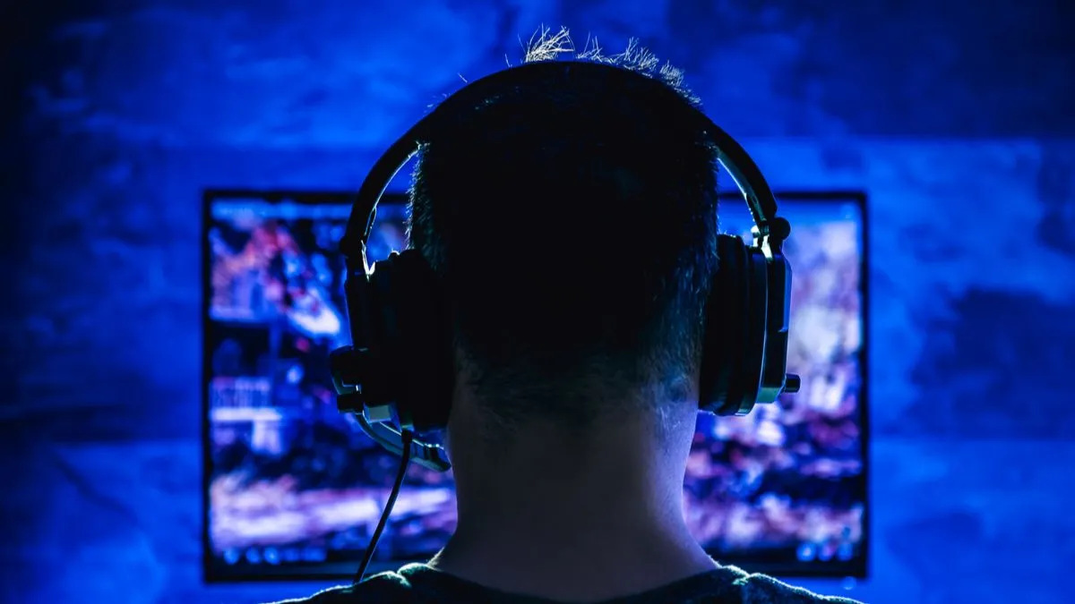 Một người đàn ông đang chơi game vào ban đêm trong không gian tối, đeo tai nghe có dây, minh họa cho việc chơi game khuya có thể khó kiểm soát.