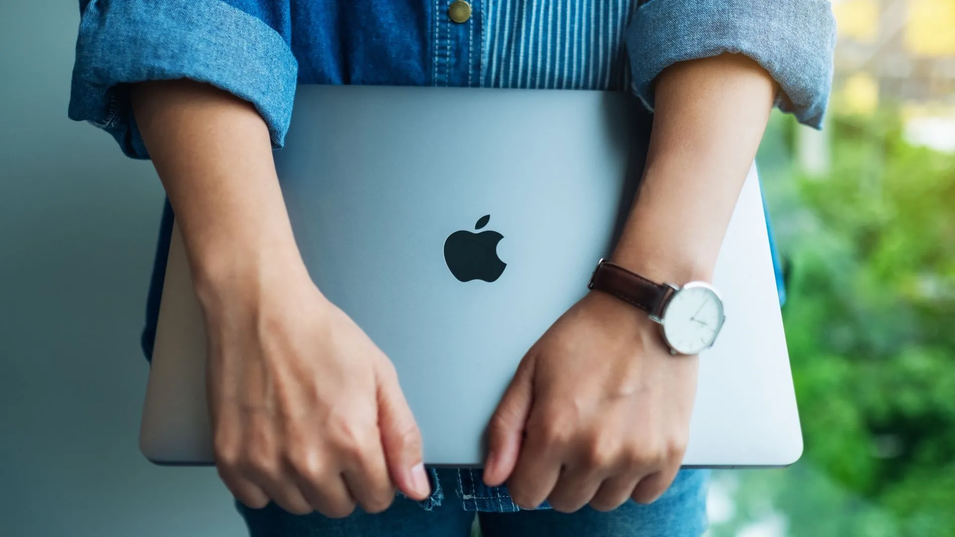 Một phụ nữ đứng cầm máy tính xách tay Apple MacBook Pro, thể hiện hình ảnh thương hiệu cao cấp của sản phẩm.