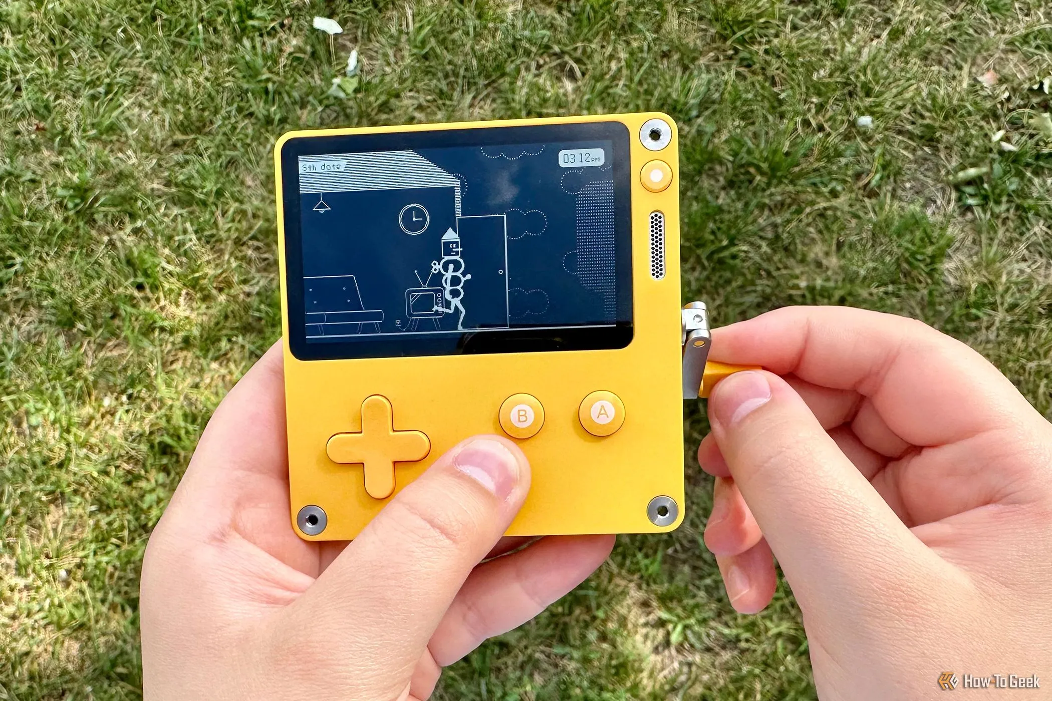 Người chơi đang dùng máy chơi game cầm tay Playdate với cơ chế tay quay bên cạnh một ly cà phê