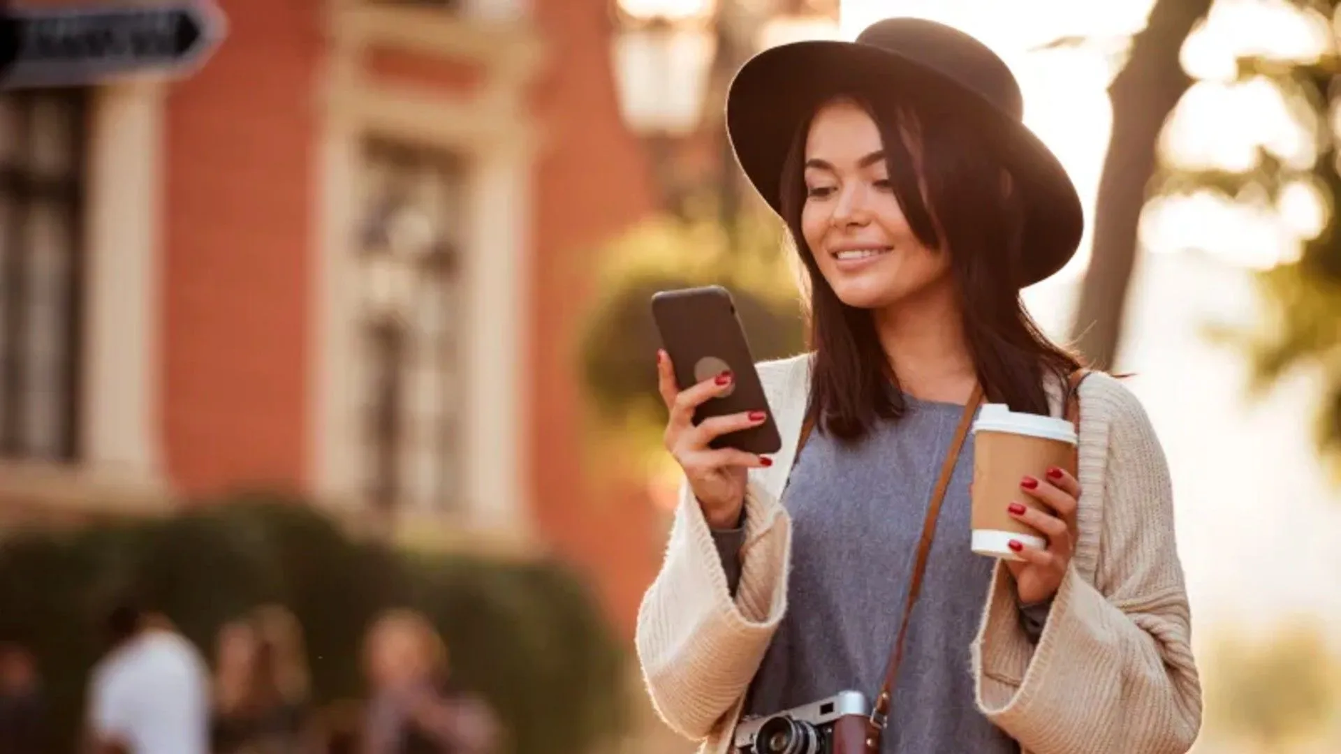Người phụ nữ đang xem điện thoại và cầm cốc cà phê