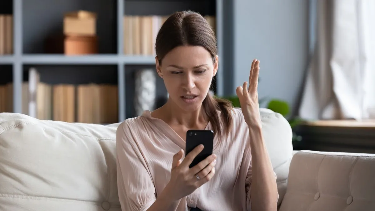 Người phụ nữ nhìn điện thoại với vẻ bối rối, thể hiện sự khó chịu với bình luận trên mạng xã hội