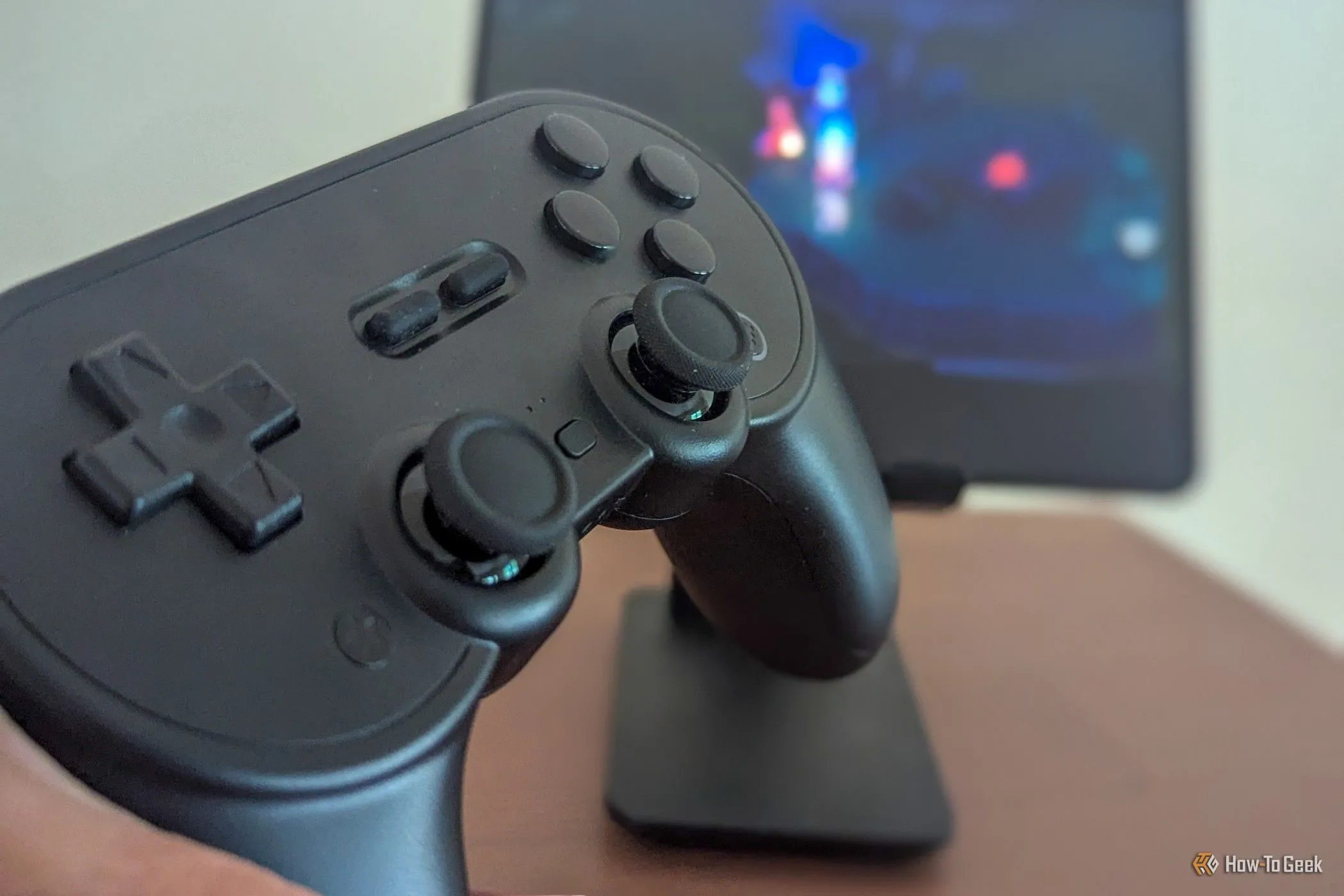 Tay cầm chơi game 8BitDo Pro 2 màu xám, với hình ảnh một game di động làm nền phía sau.