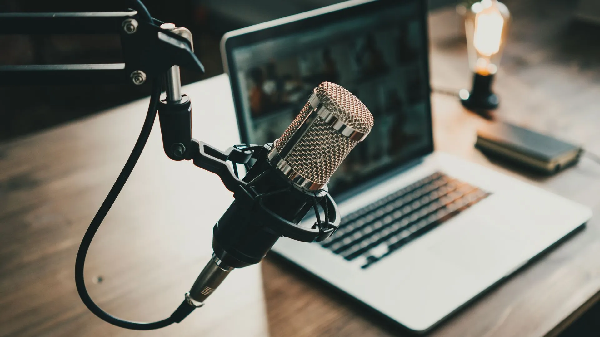 Microphone được lấy nét cận cảnh, phía sau là chiếc MacBook, tạo không gian studio tại nhà.